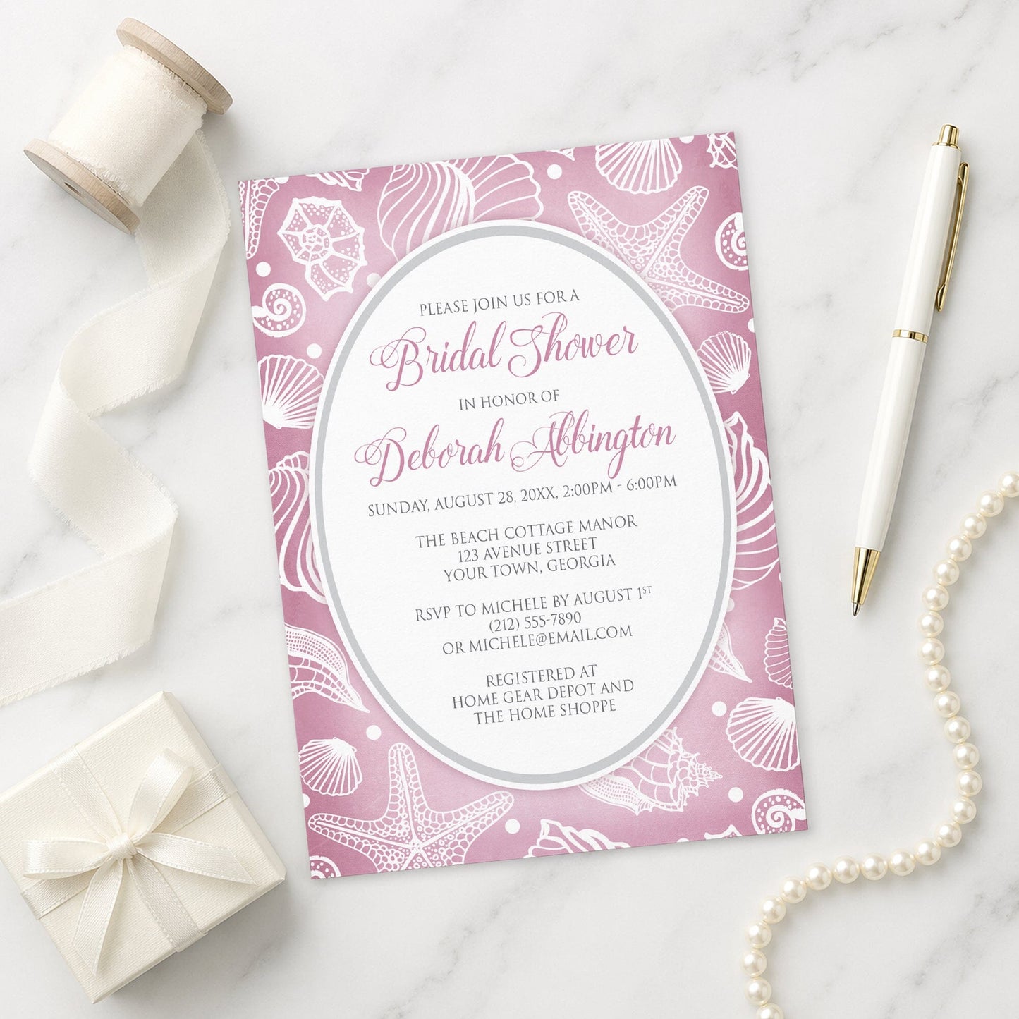 Pretty Pink Beach Seashell Bridal Shower Invitation with a pink seashell pattern shown on a marble surface with gift, pen, and pearls.