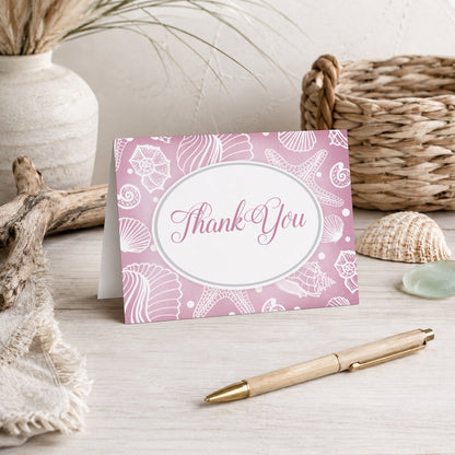 Pretty Pink Seashell Beach Thank You Card on a beach house tabletop with coastal decor and a pen.