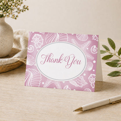 Pretty Pink Seashell Beach Thank You Card on a desk with a vase, plants, and a pen.