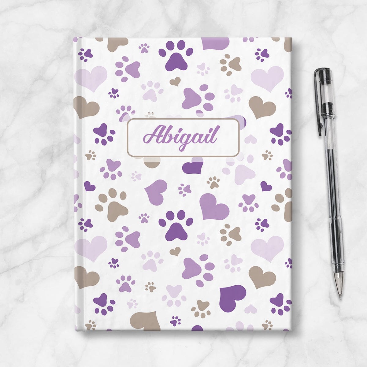 Personalized Purple Hearts and Paw Prints Journal at Artistically Invited. Image shows the book on a countertop next to a pen.