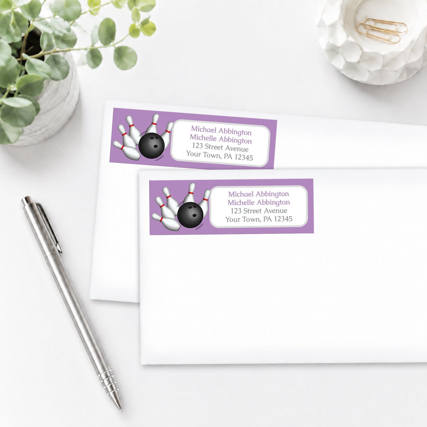 Purple Bowling Address Labels on white envelopes, shown on a white surface with a plant and a pen.