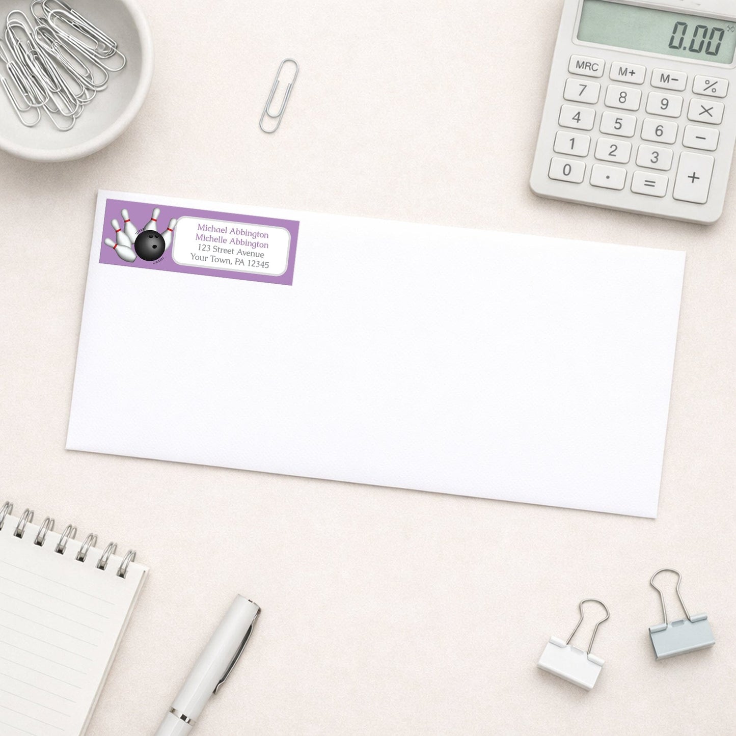 Purple Bowling Return Address Label shown on a white envelope with everyday office supplies