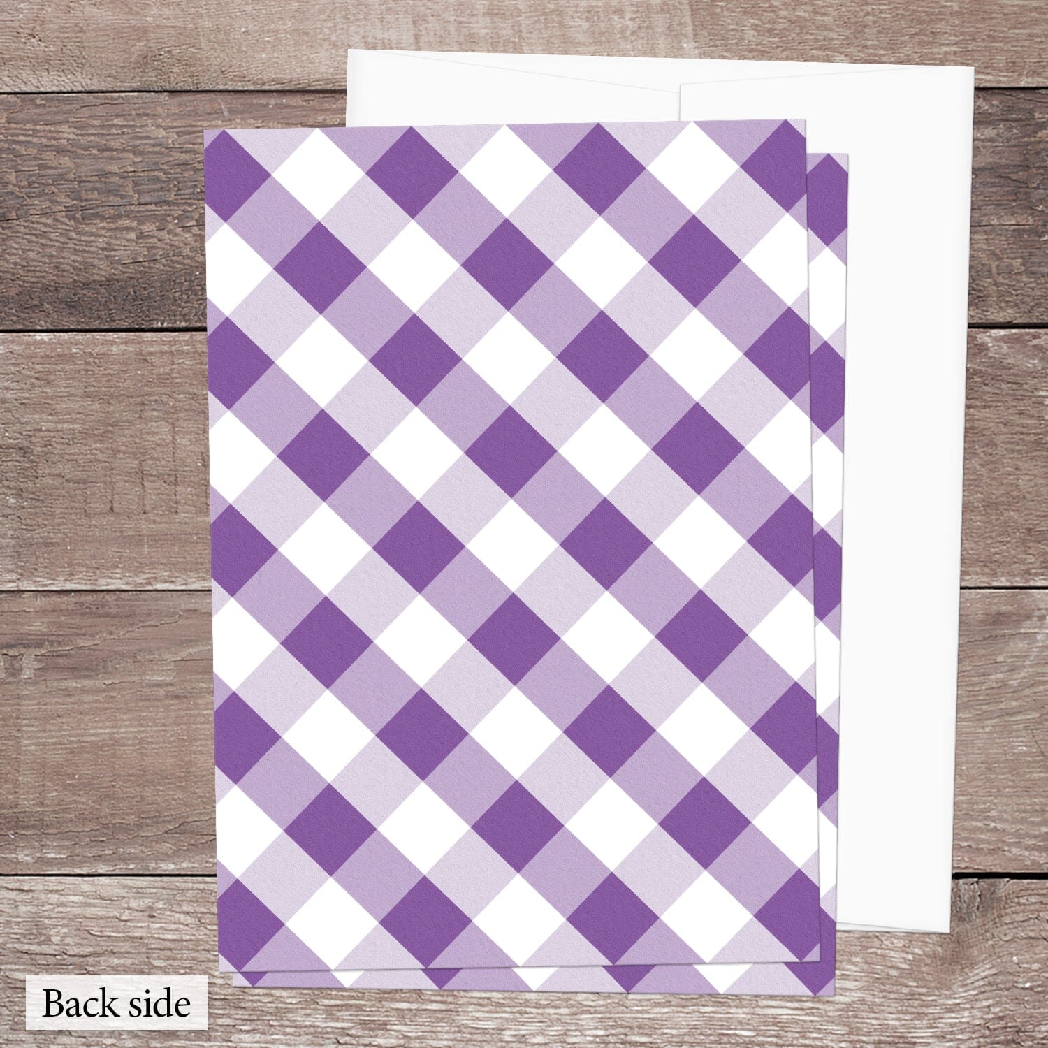 The back side of the Purple Gingham Vow Renewal Invitation, featuring the diagonal purple and white check pattern, shown on a brown wood surface with a white envelope.