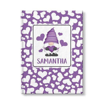 Personalized Purple Hearts Gnome Journal at Artistically Invited. A custom book designed with an adorable gnome holding a purple heart with 4 hearts floating around him in a white rectangular design on the front of the book, with your name personalized in purple in a cute all capital letters font below the gnome. The background design that wraps around the cover of the book features a purple background color filled with cute multi-directional white hearts of different sizes.