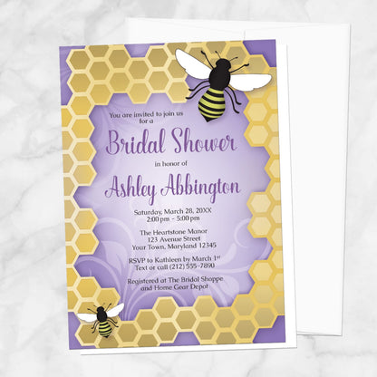 Bee bridal shower invitation with 2 bees on a honeycomb frame over a purple background, displayed with a white envelope on a marble surface