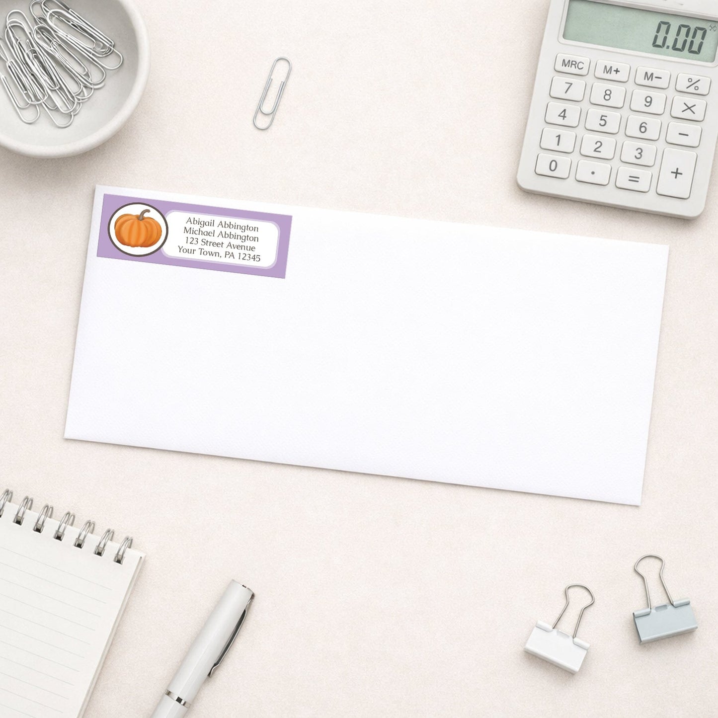 Purple Pumpkin Address Label shown on a white envelope with everyday office supplies