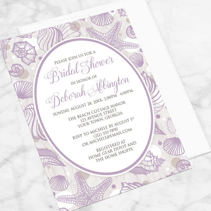 Purple Seashell Whitewashed Wood Beach Bridal Shower Invitation shown at an angle on a marble surface with a white envelope.
