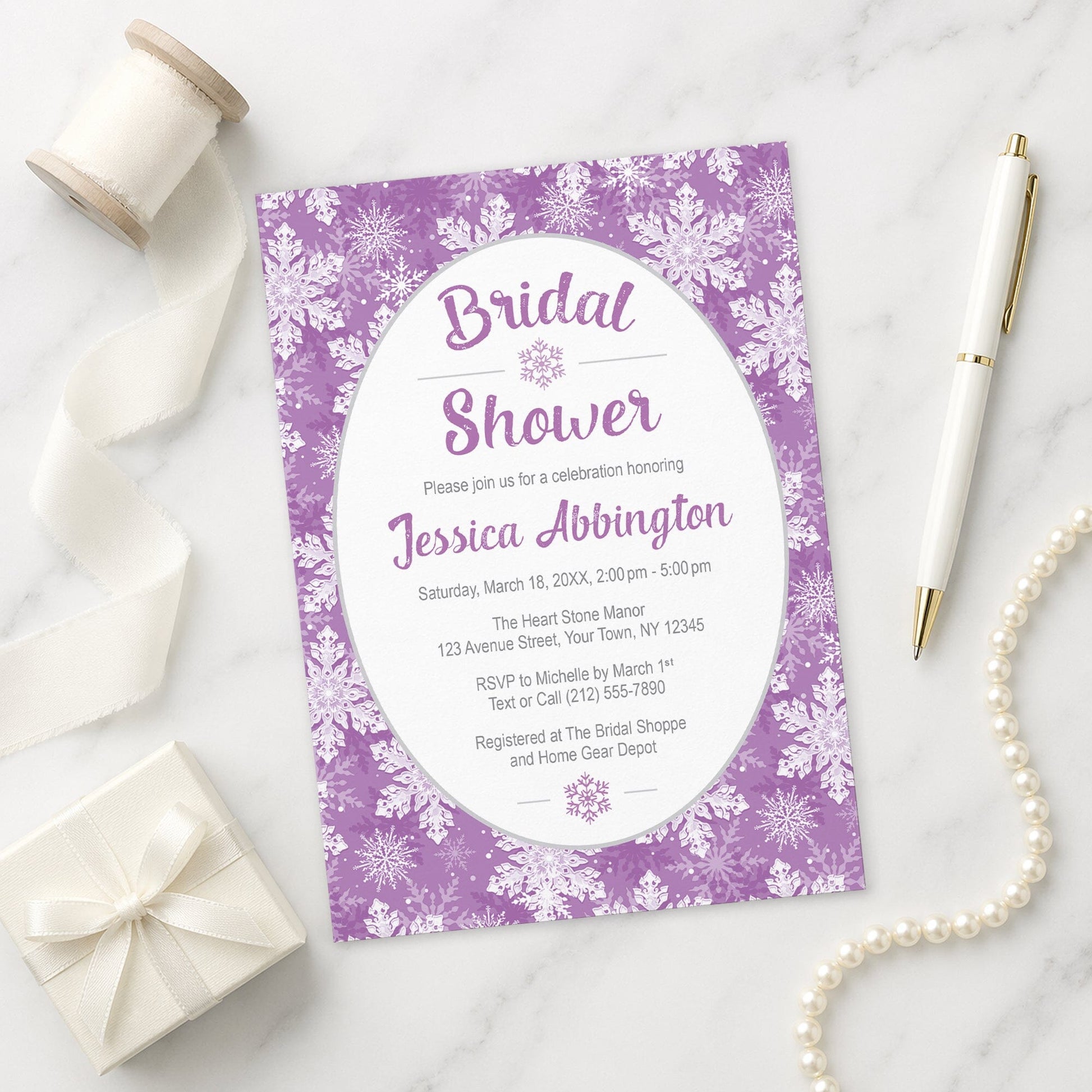 Purple Snowflake Bridal Shower Invitation shown on a marble surface with a white  gift box, pen, ribbon, and pearls.