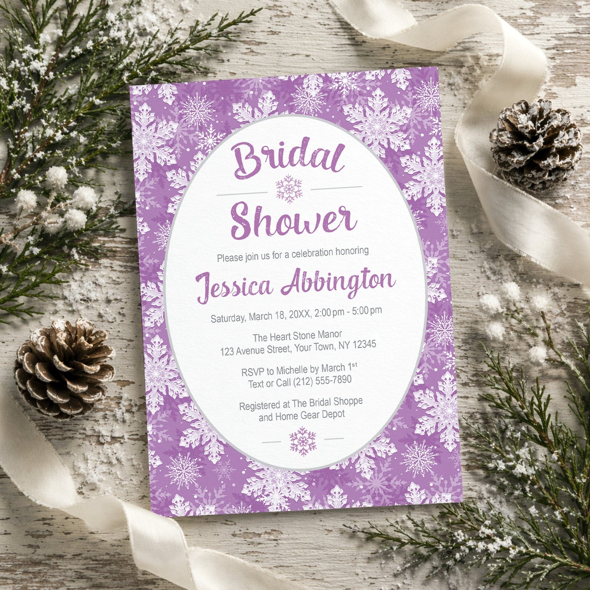Purple Snowflake Bridal Shower Invitation shown on a rustic wooden surface with winter greenery, pine cones, and ribbons.