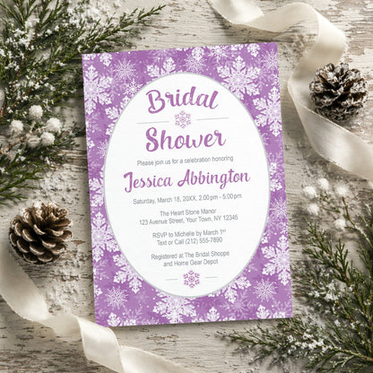 Purple Snowflake Bridal Shower Invitation shown on a rustic wooden surface with winter greenery, pine cones, and ribbons.