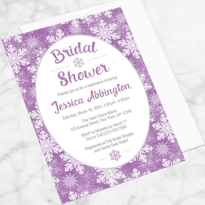Purple Snowflake Bridal Shower Invitation shown at an angle on a marble surface with a white envelope.