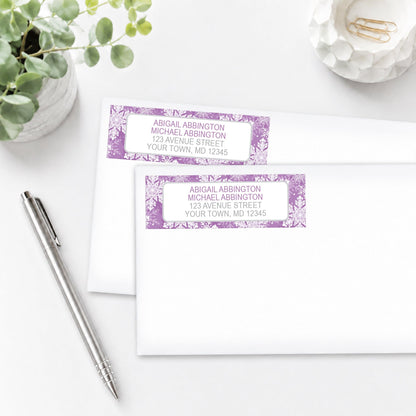 Personalized Purple Snowflake Winter Address Labels shown on white envelopes, on a white surface with a plant and a pen.