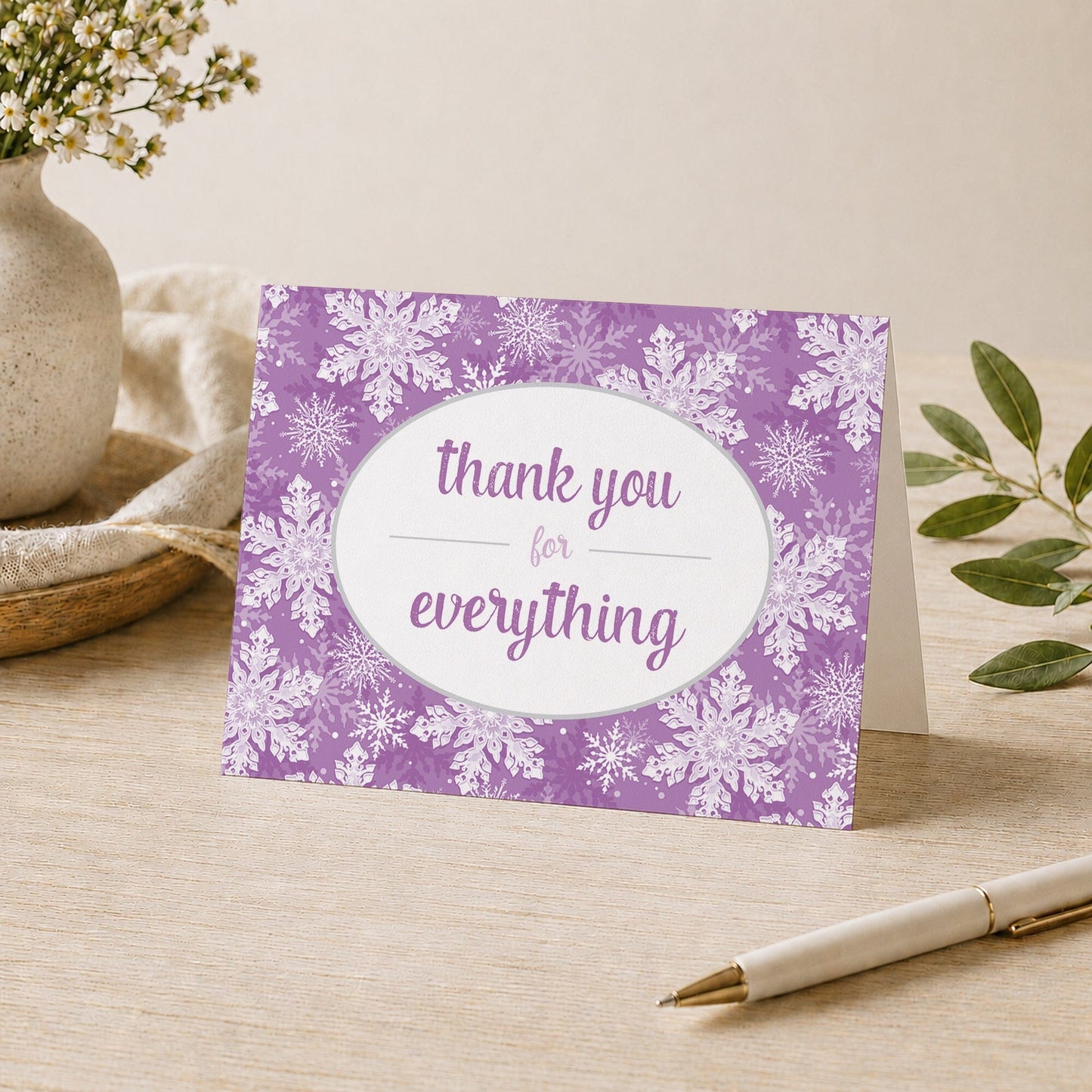 Purple Snowflake Winter Thank You Card shown on a desk with a vase, plants, and a pen.