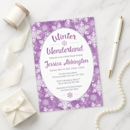 Purple Snowflake Winter Wonderland Bridal Shower Invitation shown on a marble surface with a white gift box, pen, ribbon, and pearls.