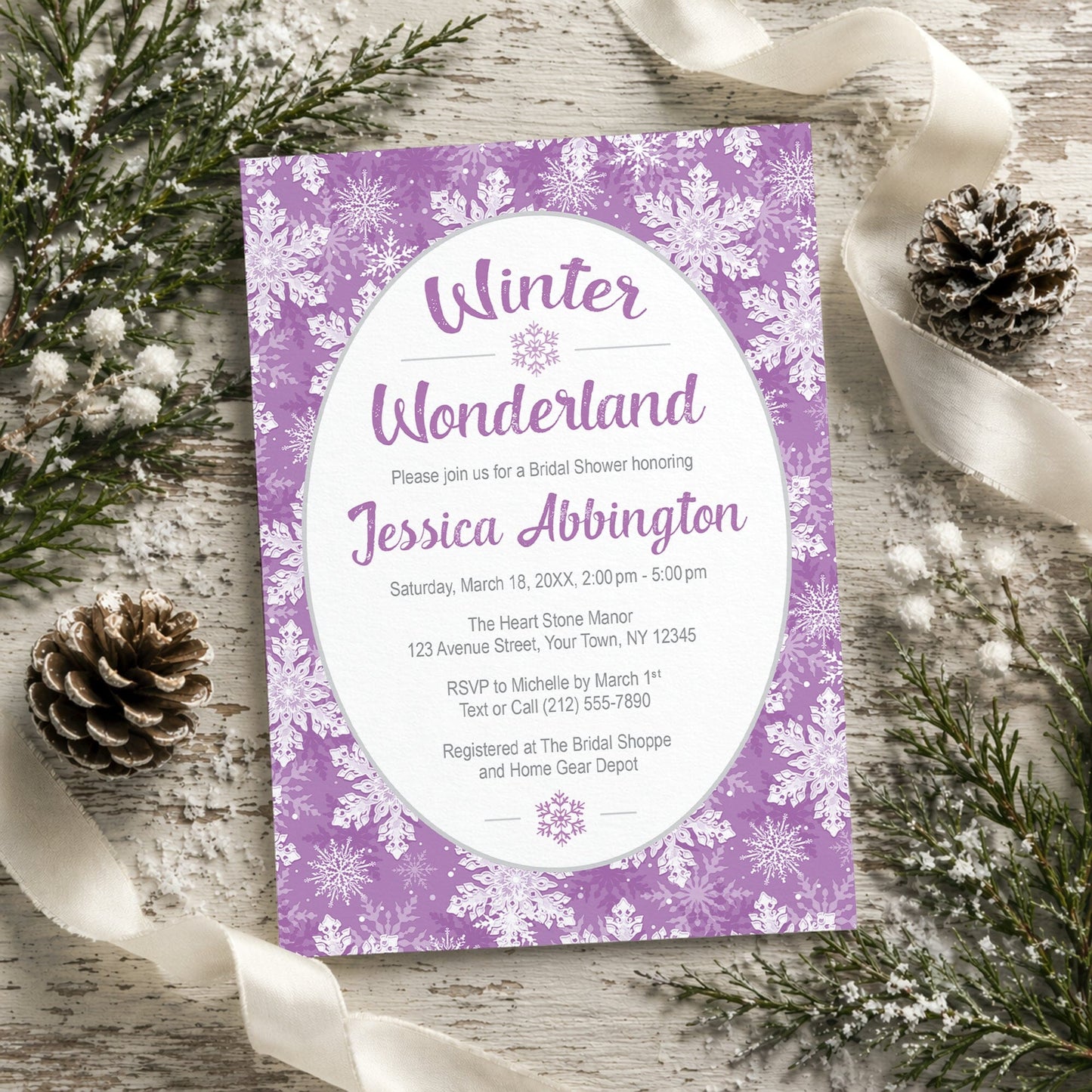 Purple Snowflake Winter Wonderland Bridal Shower Invitation shown on a rustic painted wooden surface with winter greenery, pine cones, and ribbons.