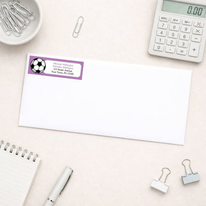 Purple Soccer Ball Return Address Label shown on a white envelope with everyday office supplies