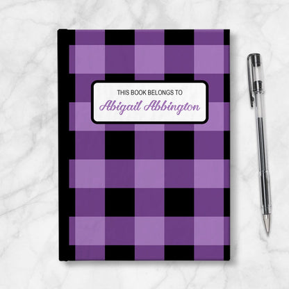 Personalized Purple and Black Buffalo Plaid Journal at Artistically Invited. Image shows the book on a countertop next to a pen.