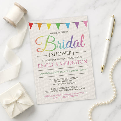 Rainbow Bunting Flags Rustic Bridal Shower Invitation shown on a marble surface with a white gift box, pen, ribbon, and pearls.