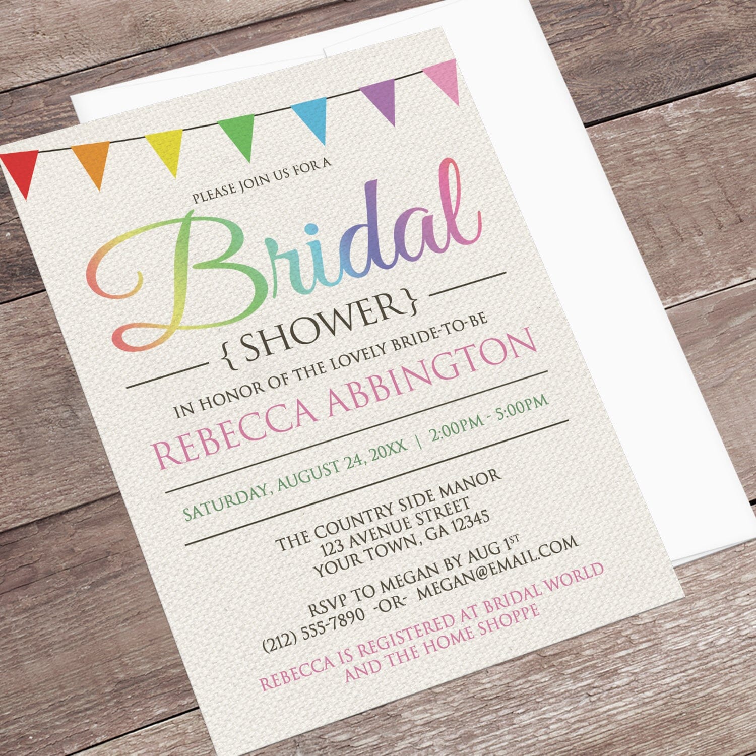 Rainbow Bunting Flags Rustic Bridal Shower Invitation shown at an angle on a wooden surface with a white envelope.