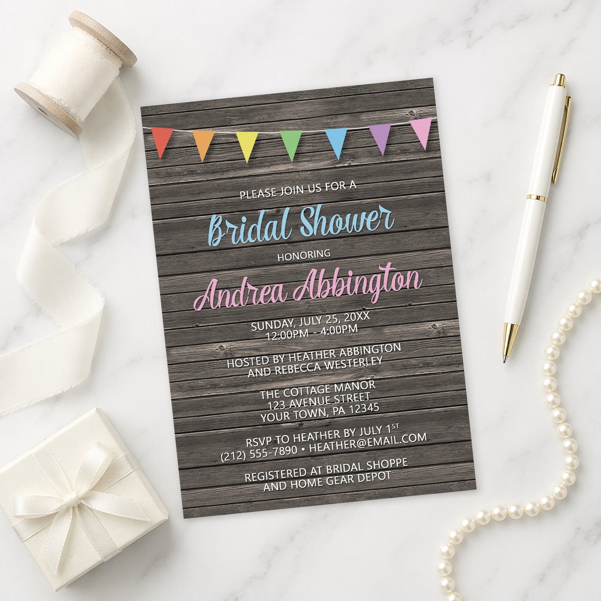 Rainbow Bunting Flags Rustic Wood Bridal Shower Invitation shown on a marble surface with a white gift box, pen, ribbon, and pearls.