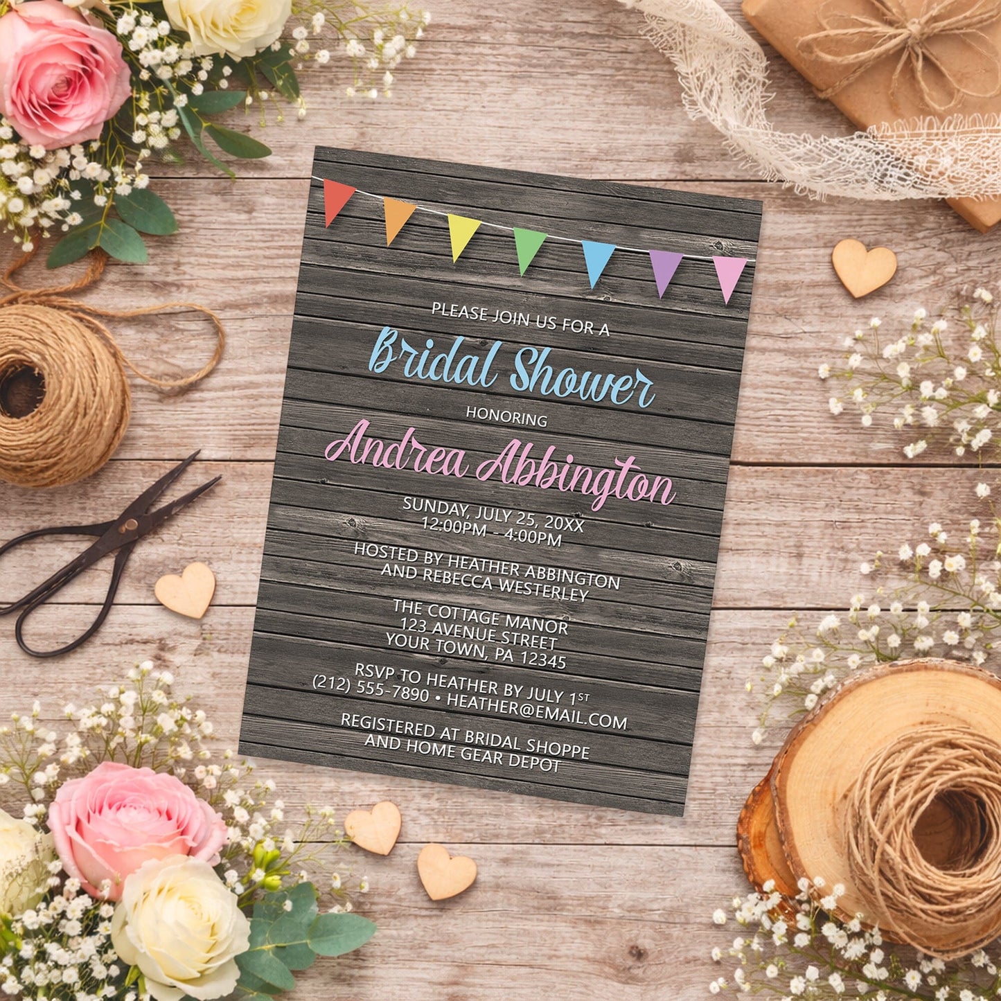Rainbow Bunting Flags Rustic Wood Bridal Shower Invitation shown on a wooden surface with spring and summer flowers, small wood hearts, lace ribbon, and twine.