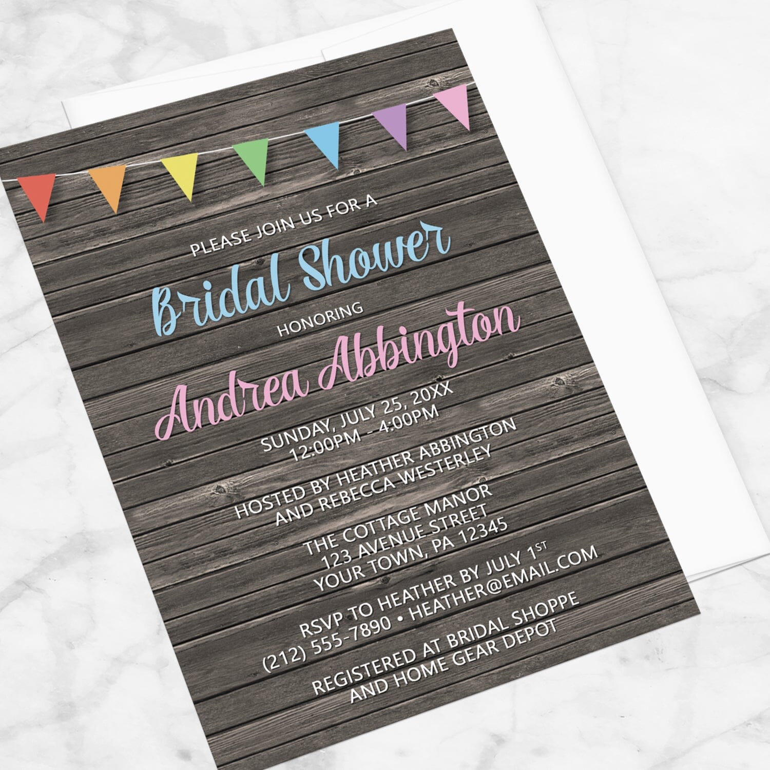 Rainbow Bunting Flags Rustic Wood Bridal Shower Invitation shown at an angle on a marble surface with a white envelope.
