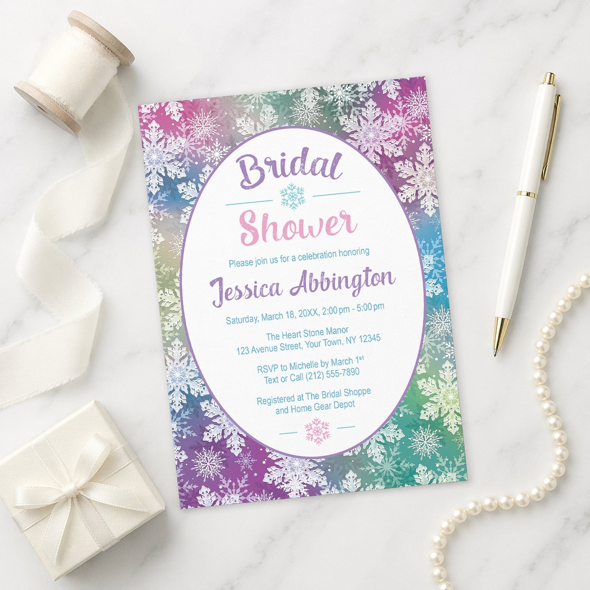 Rainbow Snowflake Bridal Shower Invitation on a marble surface with a white gift box, pen, ribbon, and pearls.