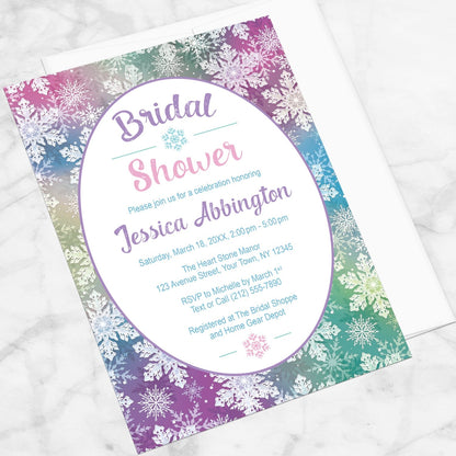 Rainbow Snowflake Bridal Shower Invitation shown at an angle on a marble surface with a white envelope.