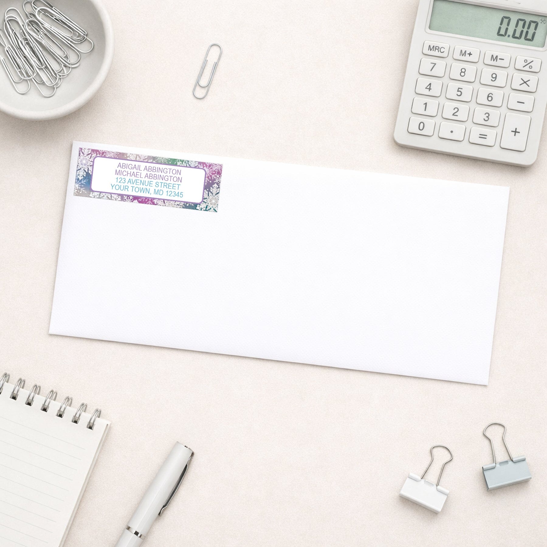 Rainbow Snowflake Winter Return Address Label shown on a white envelope with everyday office supplies
