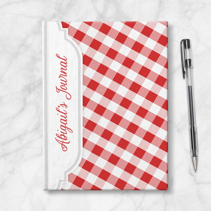 Personalized Red Gingham Journal at Artistically Invited. Image shows the book on a countertop next to a pen.