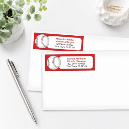 Address labels with red baseball design on envelopes with a pen and plant in the background.