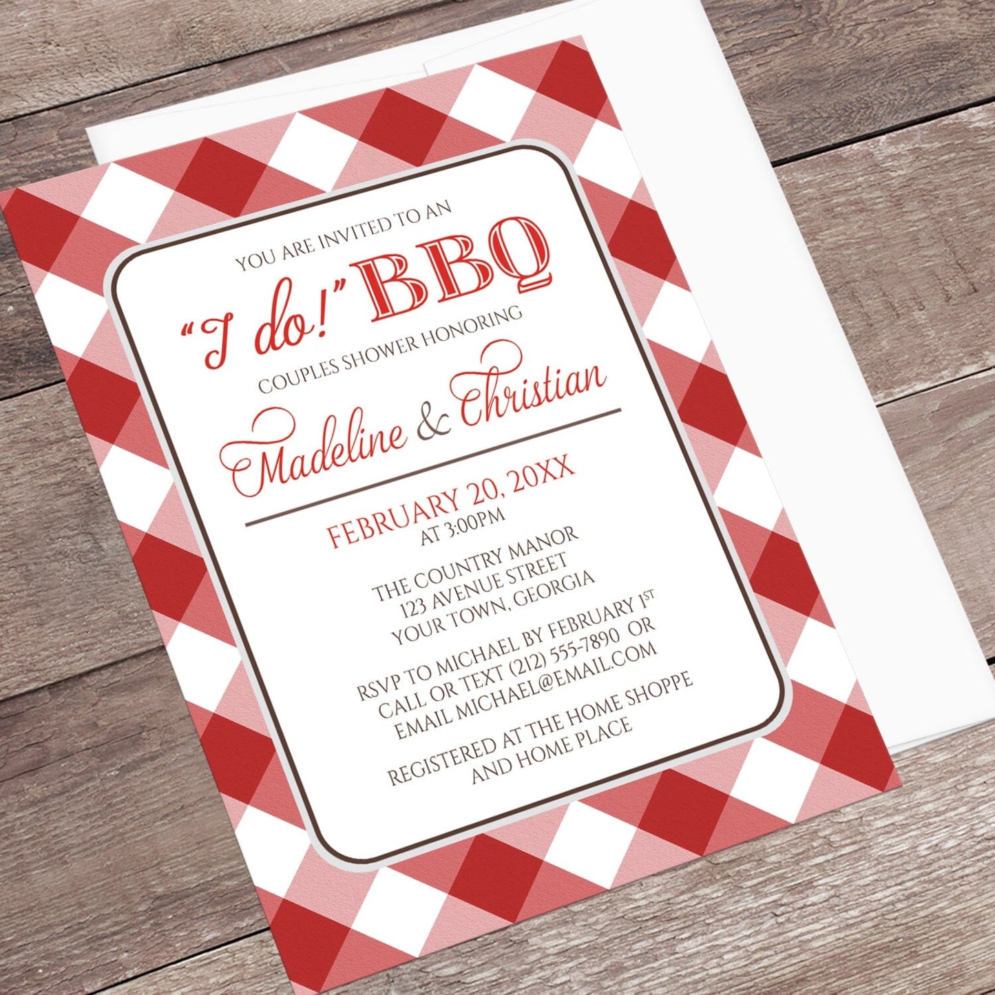 Red Gingham I Do BBQ Couples Shower Invitation shown at an angle on a brown wood surface with a white envelope.