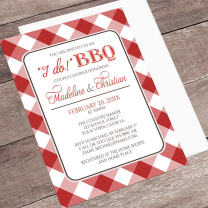 Red Gingham I Do BBQ Couples Shower Invitation shown at an angle on a brown wood surface with a white envelope.