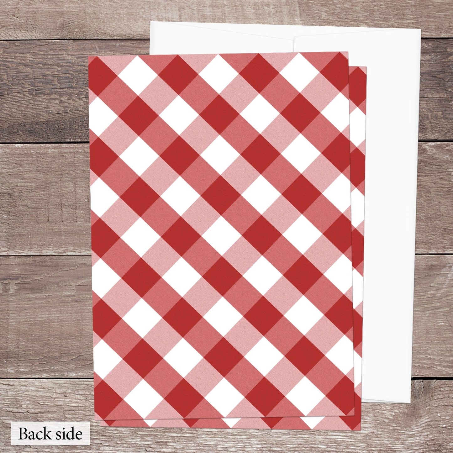 The back side of the Red Gingham Vow Renewal Invitation shown on a brown wooden surface with a white envelope.
