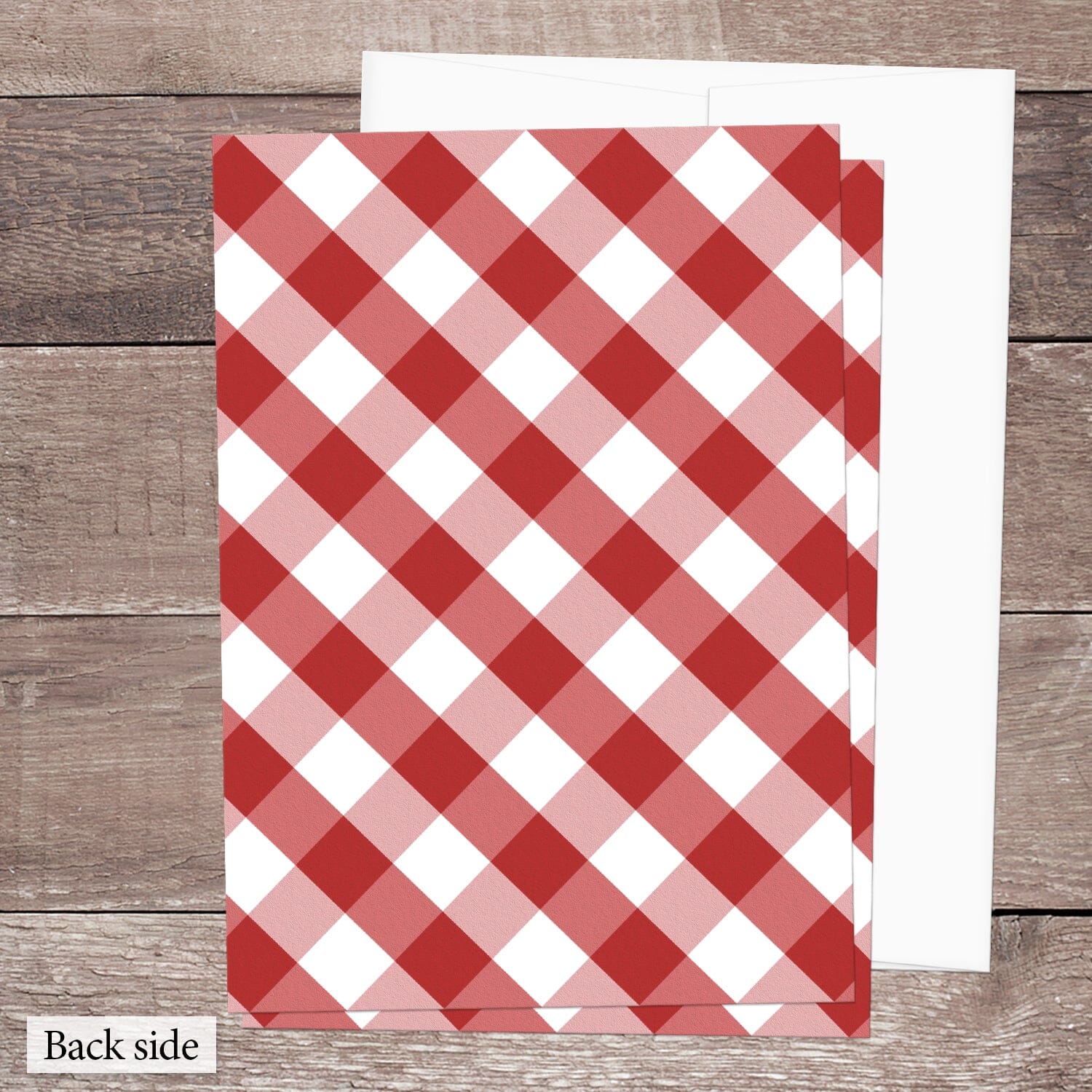 The back side of the Red Gingham Vow Renewal Invitation shown on a brown wooden surface with a white envelope.