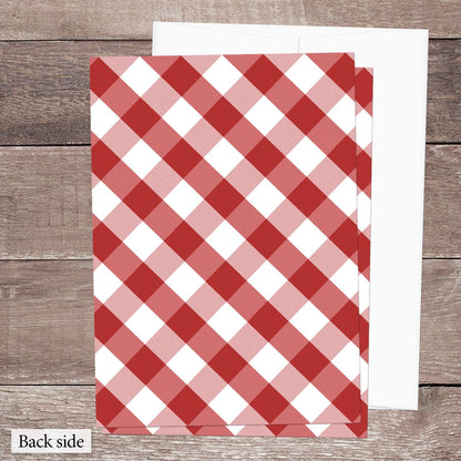 The back side of the Red Gingham Vow Renewal Invitation shown on a brown wooden surface with a white envelope.