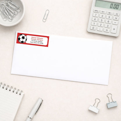 Red Soccer Ball Return Address Label shown on a white envelope with everyday office supplies