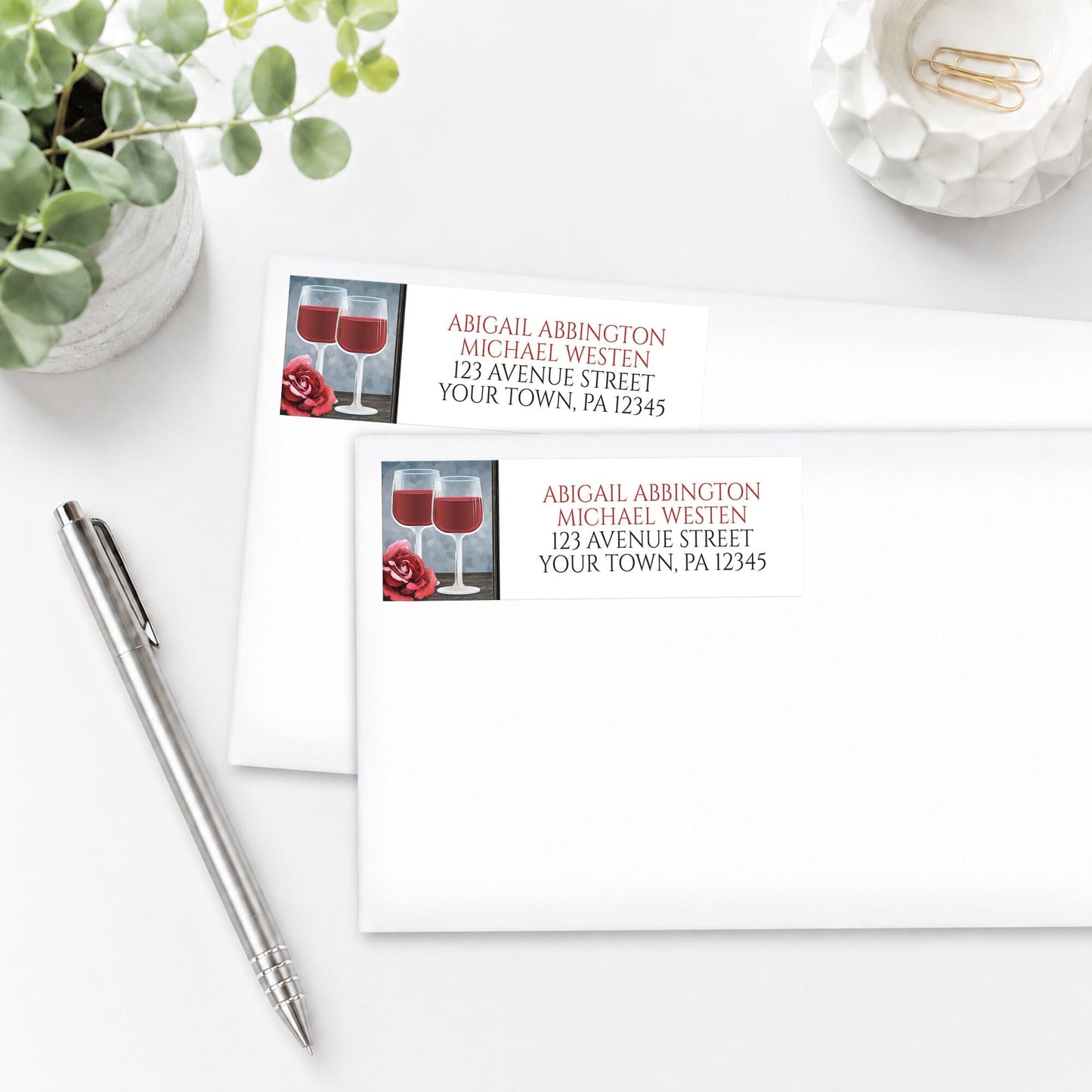 Red Wine Glasses Floral Rose Address Labels, shown on white envelopes, on a white surface with a pen and plant beside them.