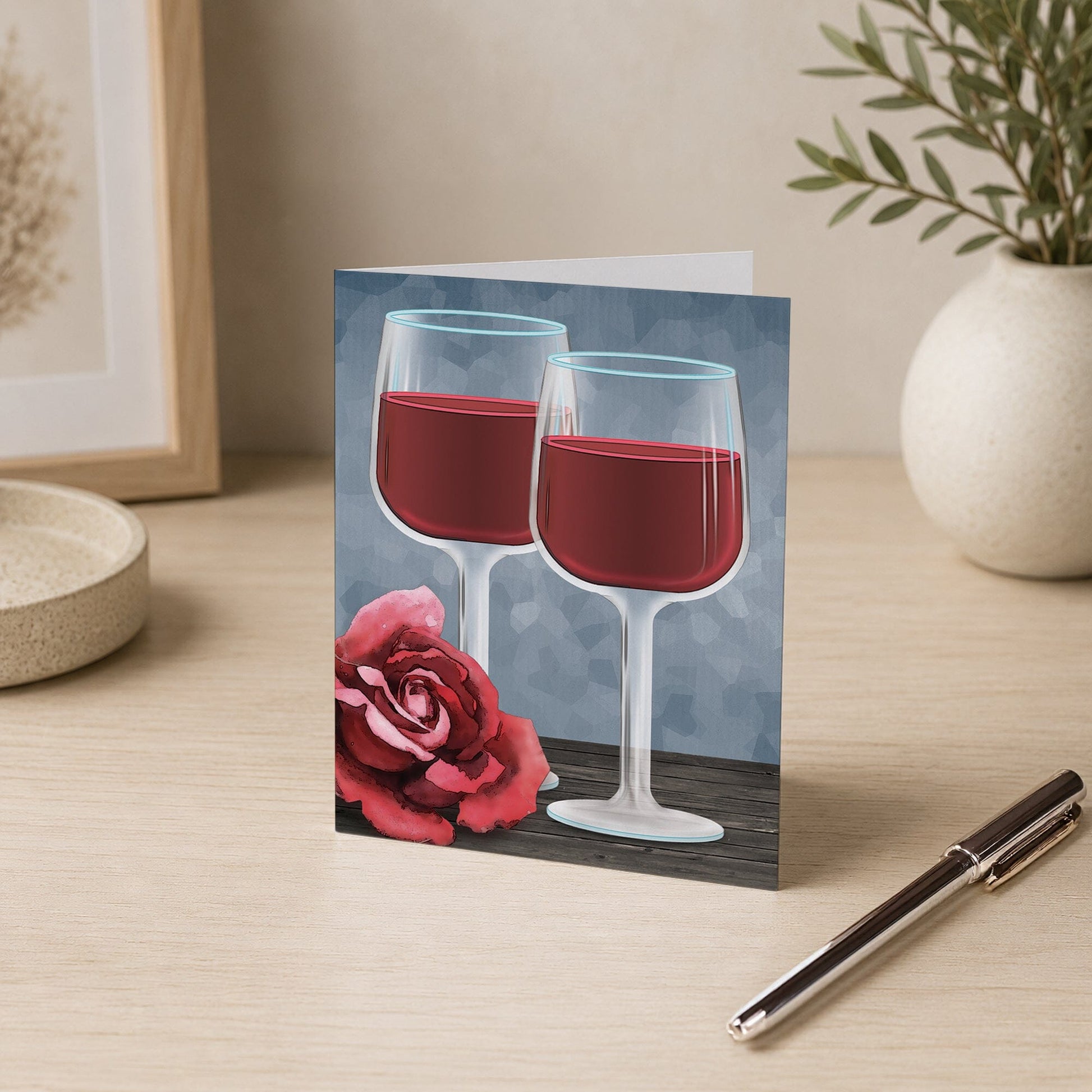 Red Wine Glasses Floral Rose Note Card shown on a desk with a vase and pen.