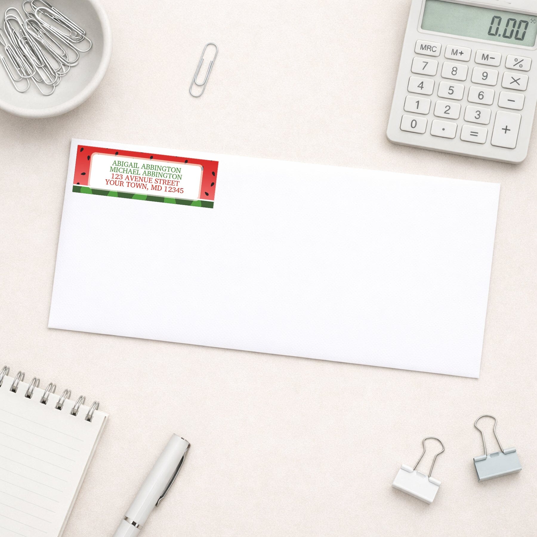 Red and Green Watermelon Address Label shown on a white envelope with everyday office supplies