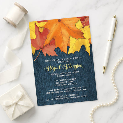Rustic Autumn Leaves Denim Bridal Shower Invitation shown on a marble surface with a white gift box, pen, ribbon, and pearls.