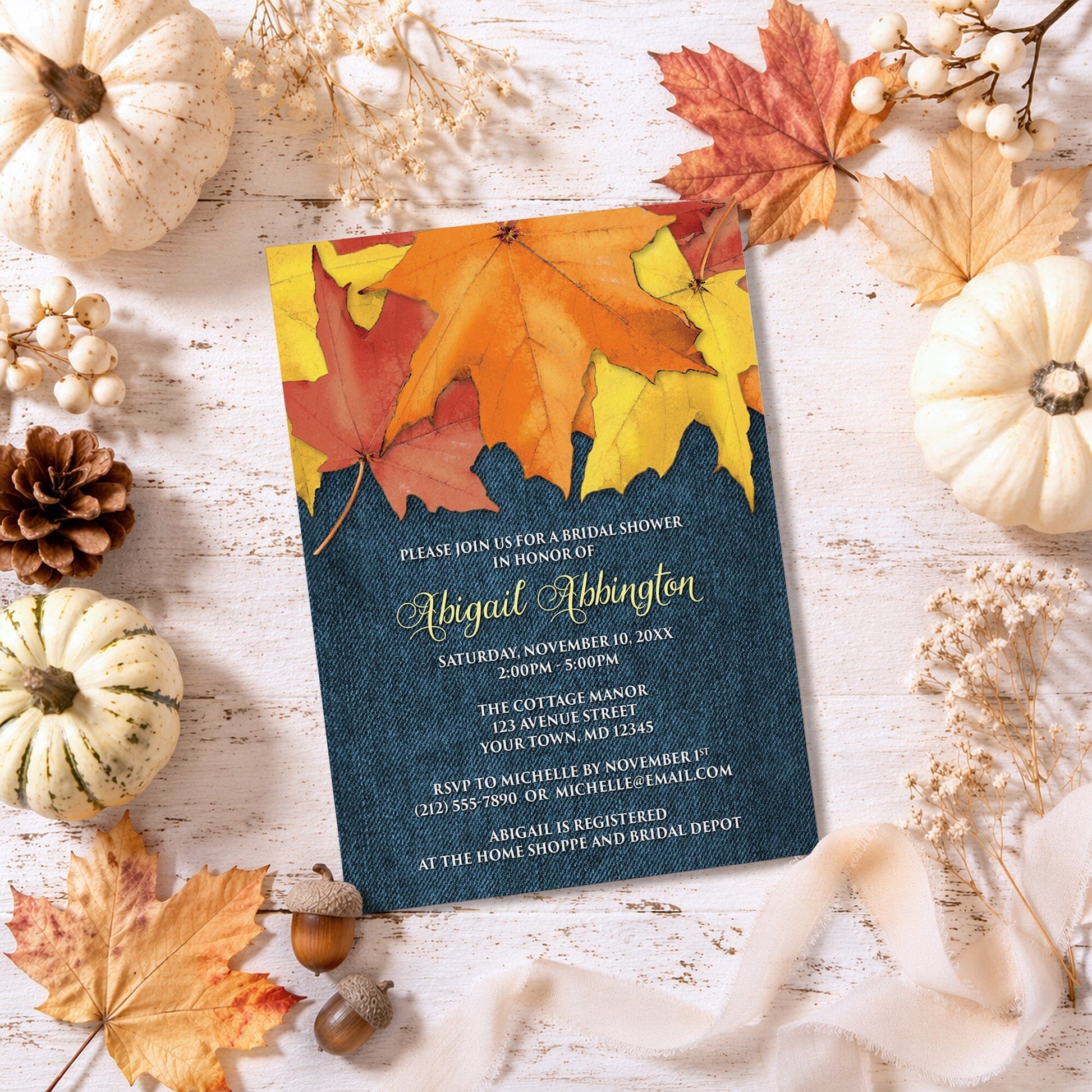 Rustic Autumn Leaves Denim Bridal Shower Invitation shown on a painted wooden surface with fall leaves and autumn decor.