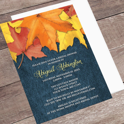 Rustic Autumn Leaves Denim Bridal Shower Invitation shown at an angle on a wooden surface with a white envelope.