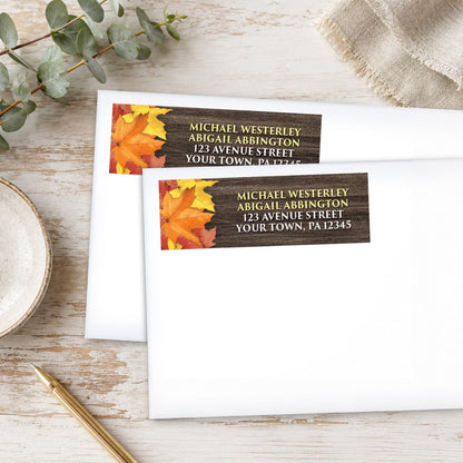 Two Rustic Autumn Leaves Wood Address Labels with a fall leaf design, shown on white envelopes, with a pen and eucalyptus branch on a wooden surface.