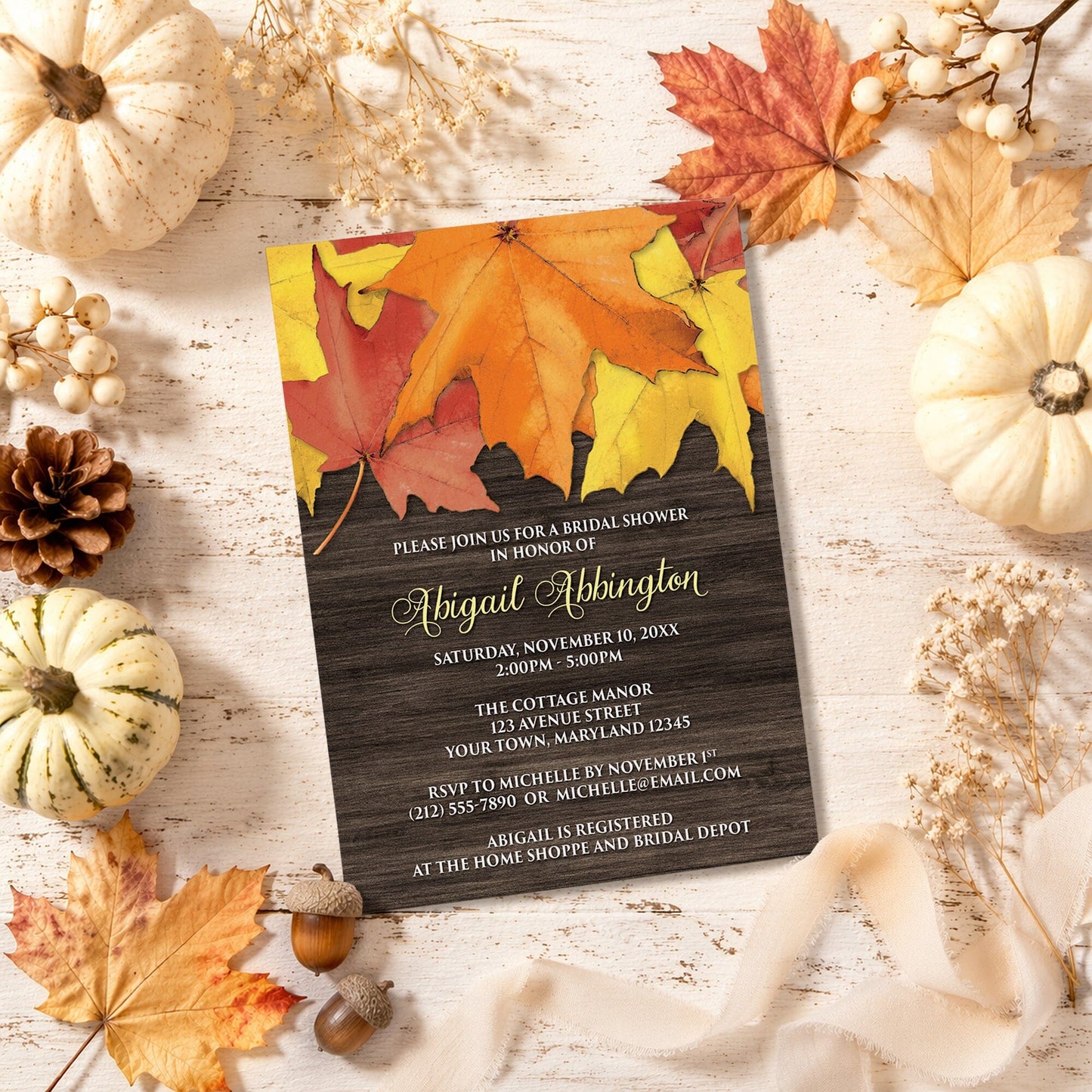 Rustic Autumn Leaves Wood Bridal Shower Invitation shown with leaves and pumpkins on a wooden surface