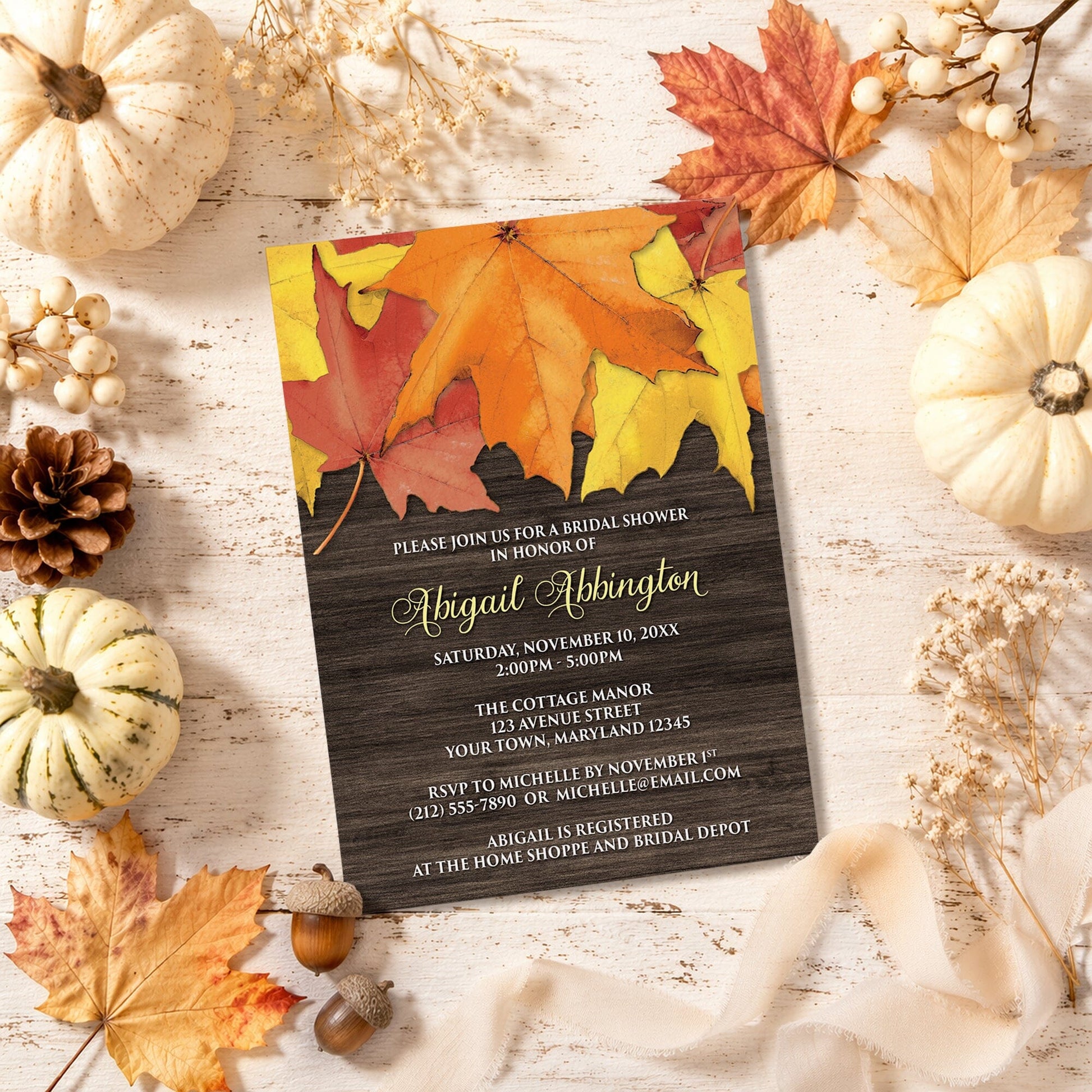 Rustic Autumn Leaves Wood Bridal Shower Invitation shown with leaves and pumpkins on a wooden surface