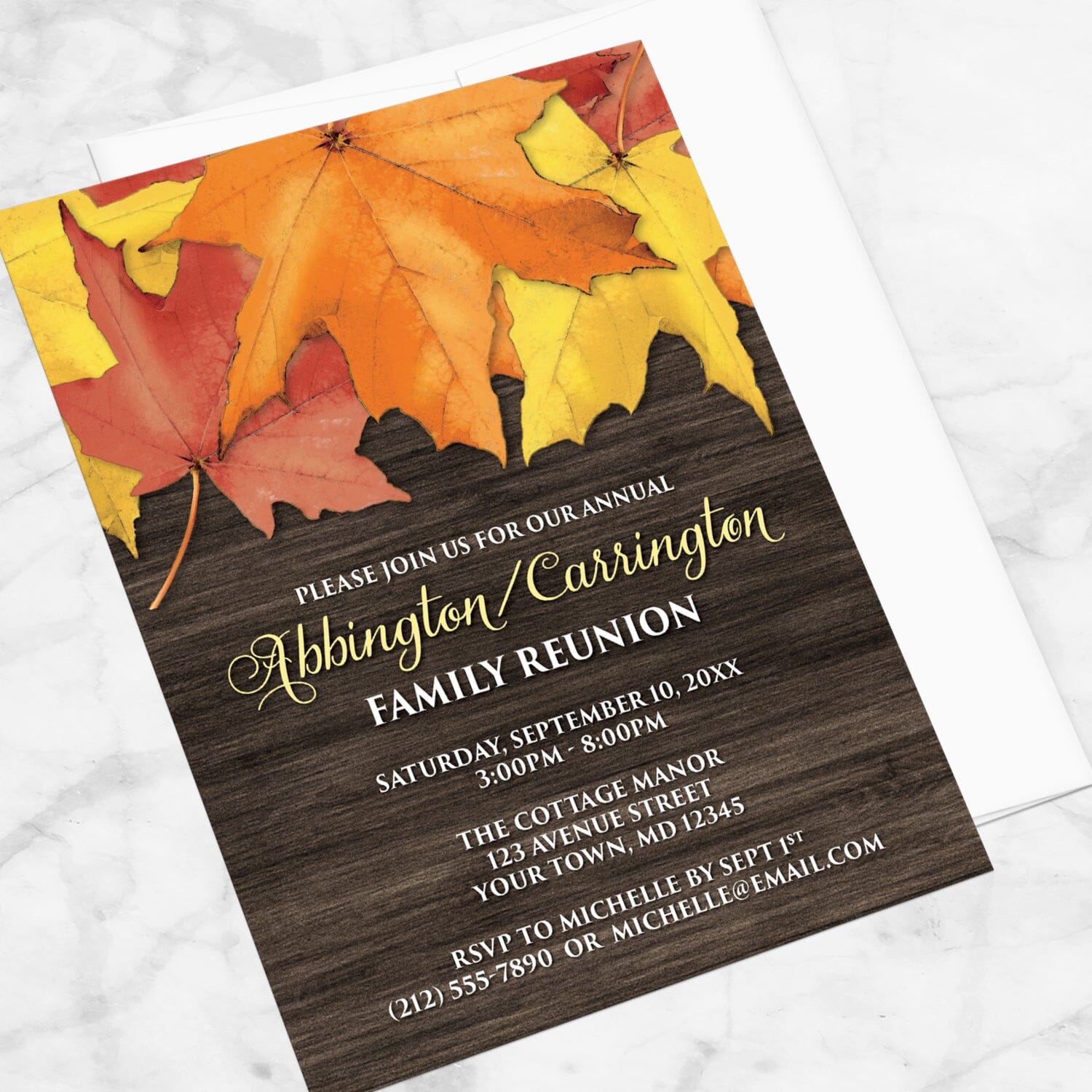 Rustic Autumn Leaves Wood Family Reunion Invitation shown at an angle on a marble surface with a white envelope.