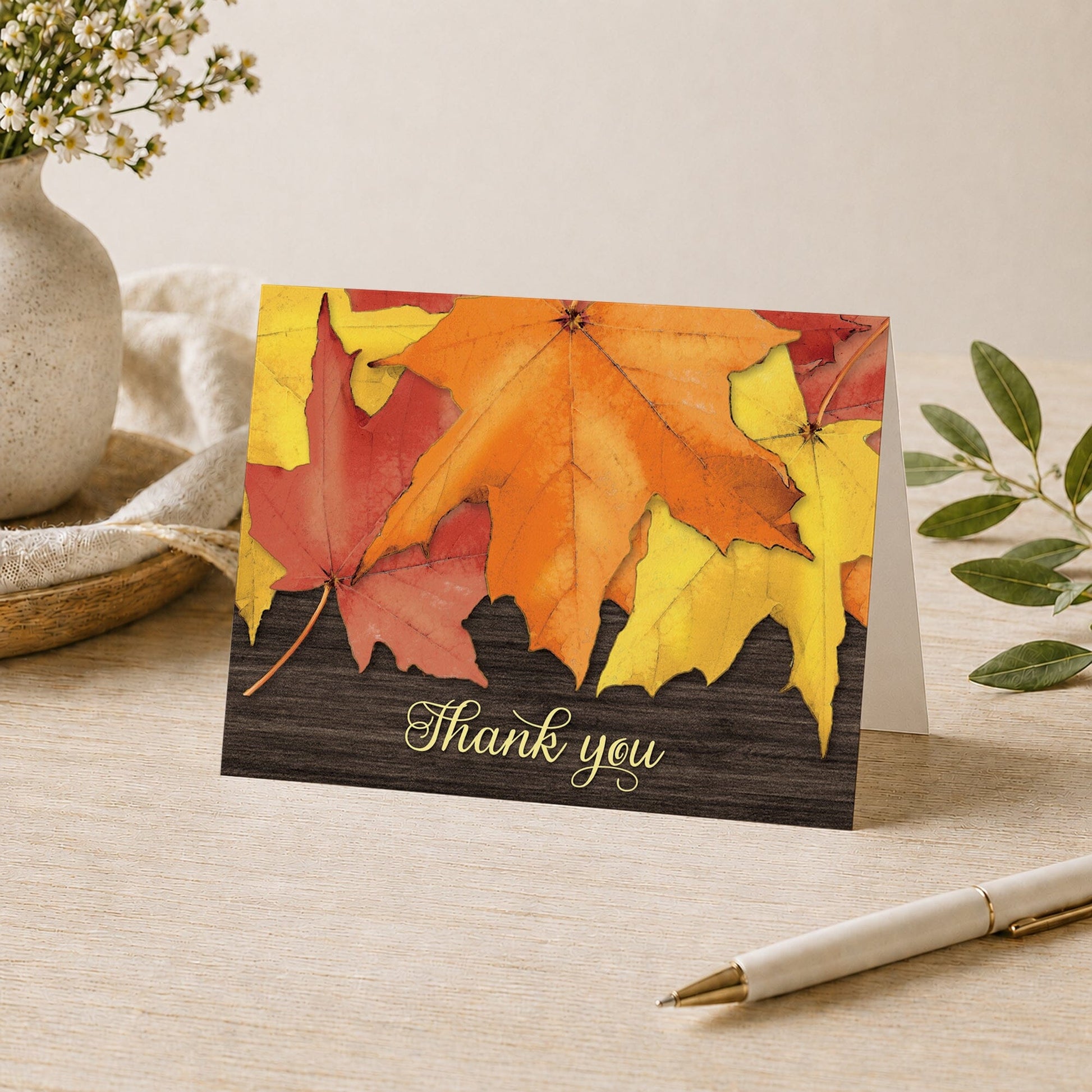 Rustic Autumn Leaves Wood Thank You Card shown on a desk with a vase, plants, and a pen.