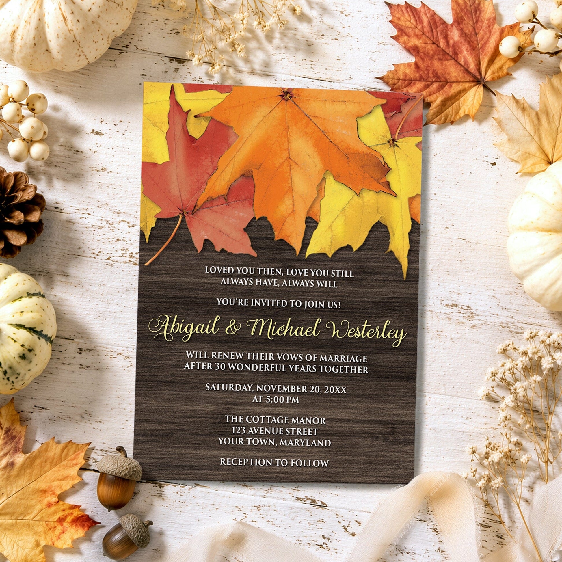 Rustic Autumn Leaves Wood Vow Renewal Invitation shown on a light wooden surface with fall leaves, small pumpkins, and autumn decor.