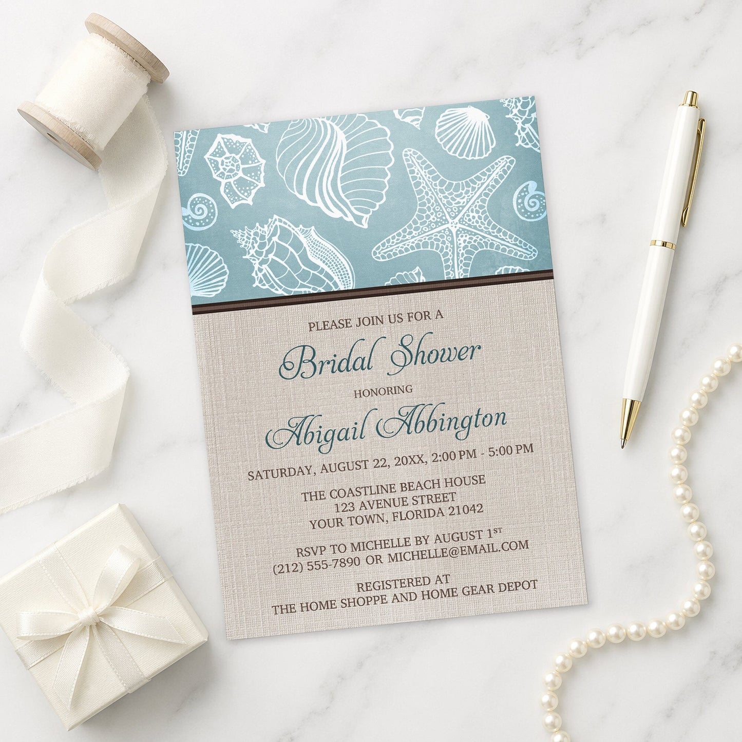 Rustic Beach Linen Seashell Bridal Shower Invitation shown on a marble surface with decorative items.